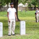 performer Andrew Davis, in khakis and white t-shirt, sings at the graves of soldiers of the 24th US Infantry who lost their lives during the 1917 Camp Logan Uprising. Part of Jefferson Pinder's performance, Fire and Movement.