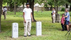 performer Andrew Davis, in khakis and white t-shirt, sings at the graves of soldiers of the 24th US Infantry who lost their lives during the 1917 Camp Logan Uprising. Part of Jefferson Pinder's performance, Fire and Movement.
