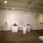 Photo of exhibition space with multiple camera sculptures, and photographs on wall.